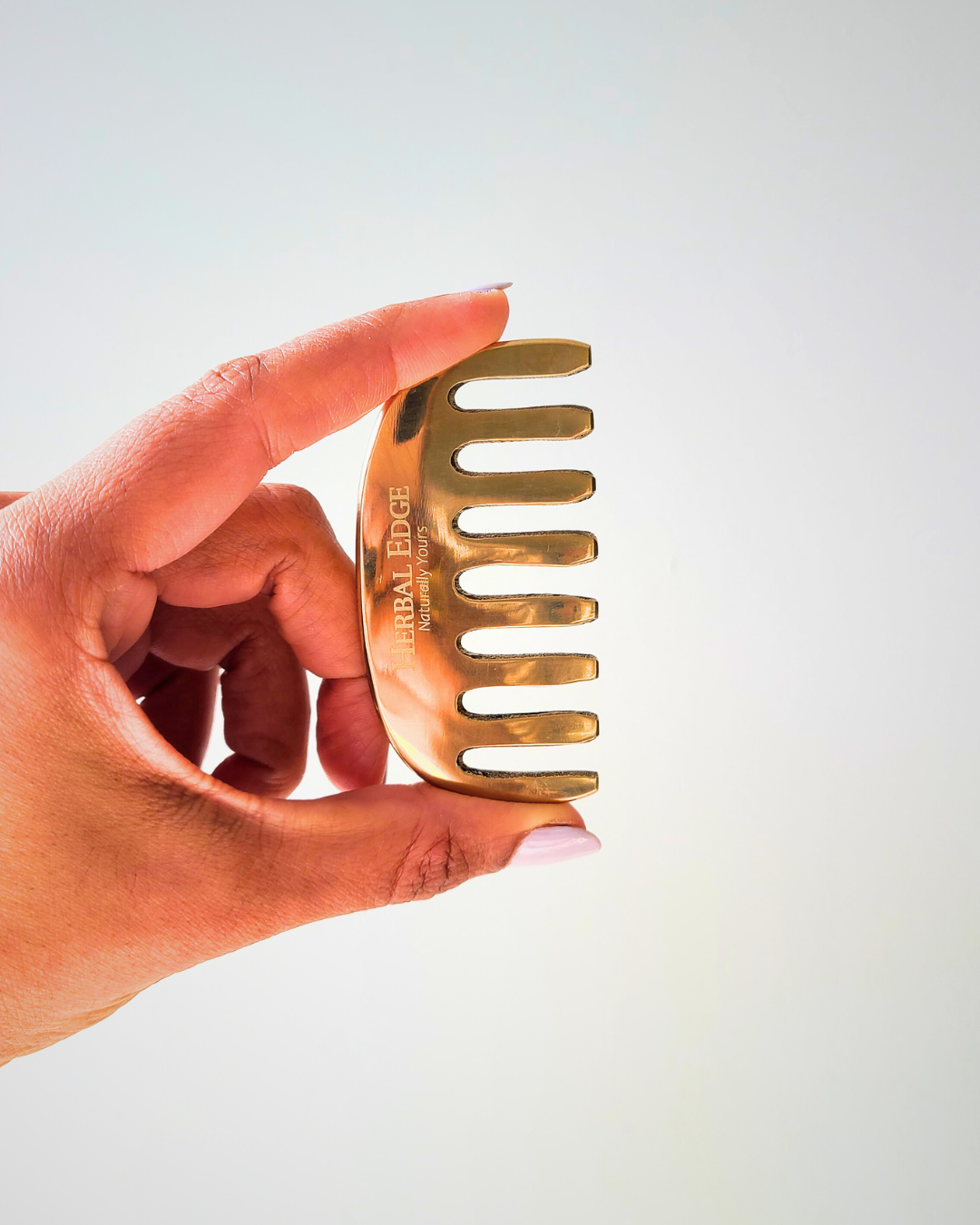 Hand holding a gold wide-tooth comb against a light background